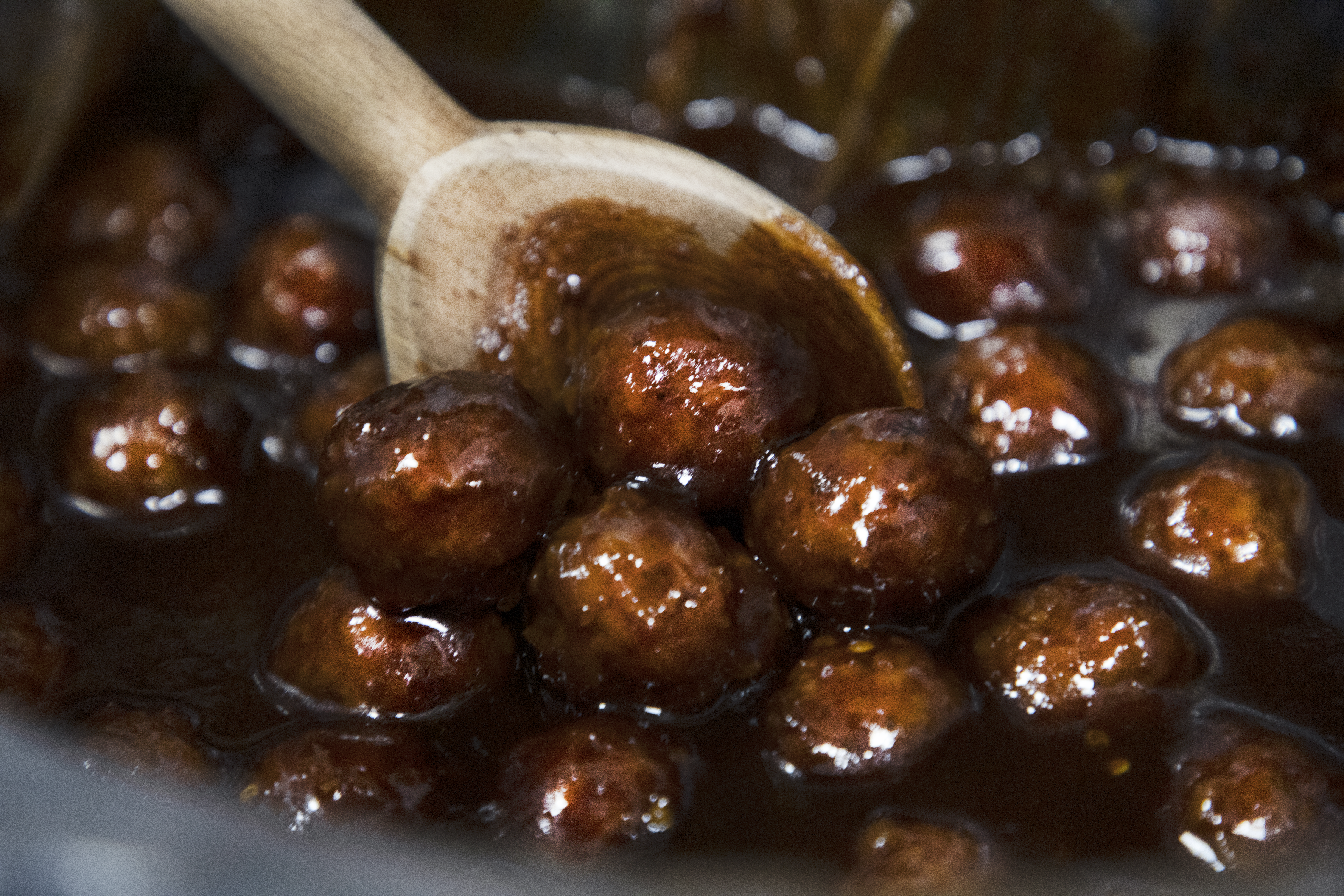 meatballs covered in barbeque sauce being stirred with a wooden spoon