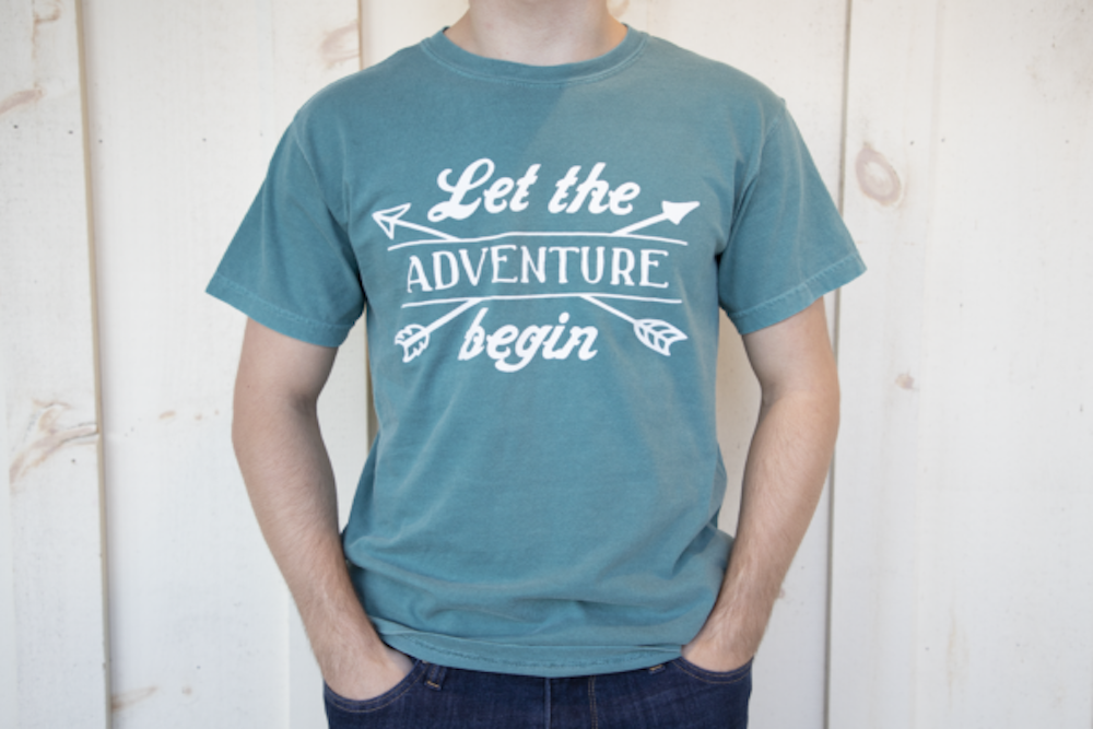 man wearing an emerald t-shirt that reads "let the adventure begin"
